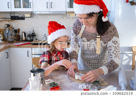 Mom and daughter in the white kitchen are preparing cookies for Christmas and new year. Family day, preparation for the holiday, learn to cook delicious pastries, cut shapes out of dough with molds 109682019