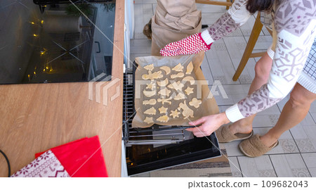 Mom puts cut-out cookies in the oven from the dough with molds on a Christmas theme in the form of a snowman, a Christmas tree, stars 109682043