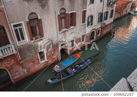 A serene scene of a blue gondola floating down a canal in Venice, Italy. The empty gondola adds to the tranquility, with picturesque buildings lining the waterway. 109682287
