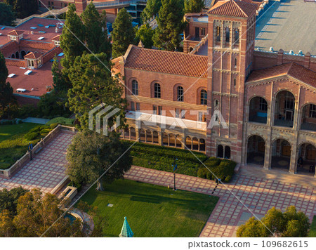 Aerial view of a Romanesque Revival university building with a tower, arched windows, and a grand entrance, surrounded by manicured lawns and pathways in the USA. 109682615