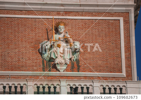 Statue of a woman seated on a throne with lions on a building in Venice, Italy. Explore the beauty of Venice in the summer with our collection. 109682673