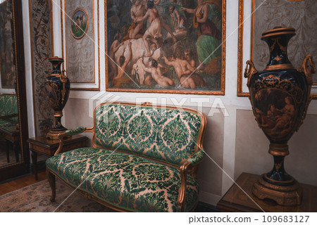 Experience the opulence and grandeur of a Venetian-inspired room with ornate couches, vases, and paintings. The green and gold color scheme creates a luxurious and elegant ambiance. Experience the opulence and grandeur of a Venetian-inspired room with ornate couches, vases, and paintings. The green and gold color scheme creates a luxurious and elegant ambiance. 109683127