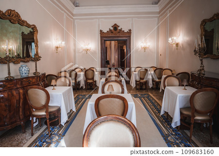 Elegant and ornate dining room with tables and chairs. The decor is inspired by an unknown era, with no specific landmarks or lighting fixtures visible. Elegant and ornate dining room with tables and chairs. The decor is inspired by an unknown era, with no specific landmarks or lighting fixtures visible. 109683160