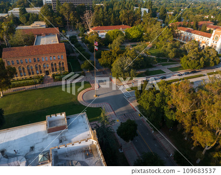 Aerial view of a vibrant university campus with red-brick and modern buildings, a domed library, lush greenery, pathways, and an American flag, on a sunny day. Aerial view of a vibrant university campus with red-brick and modern buildings, a domed library, lush greenery, pathways, and an American flag, on a sunny day. 109683537