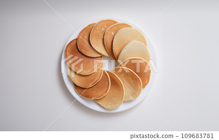 Plate with many round pancakes standing on white background top view Plate with many round pancakes standing on white background top view 109683781
