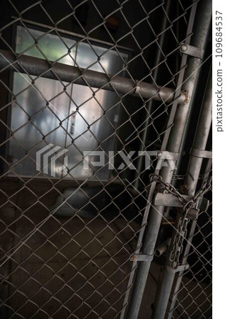 Padlocked chain link fence blocks steel door with human silhouette 109684537