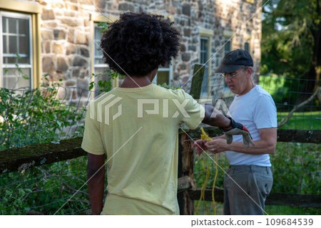 Caucasian father and African American son repair storm damaged fence 109684539