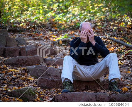 Man sits on outdoor stone steps covering his face sad 109684694