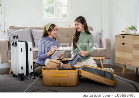 Asian beautiful tourists two women friend help collect clothes and supplies. Young female traveler feeling happy and enjoy, prepare luggage and ready for holidays vacation trip together 109688493