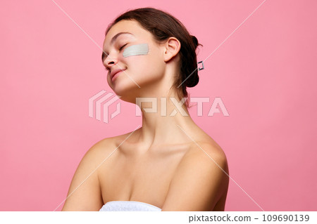 Pretty, tender young girl with face mask on skin standing in shower towel against pink background. Nourishing products Pretty, tender young girl with face mask on skin standing in shower towel against pink background. Nourishing products 109690139