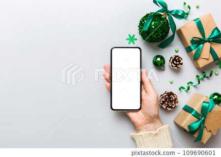 christmas mockup with space for text. christmas advertising, app template. hand holding phone with empty screen on table background. Happy New Year and Xmas Flat lay 109690601