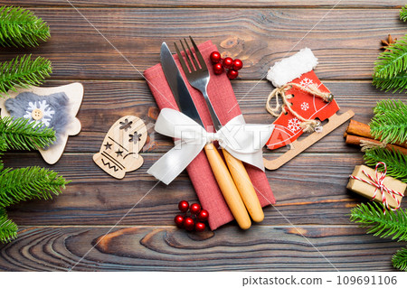 Top view of christmas decorations on wooden background. Close up of fork and knife on napkin tied up with ribbon. New year pattern concept 109691106