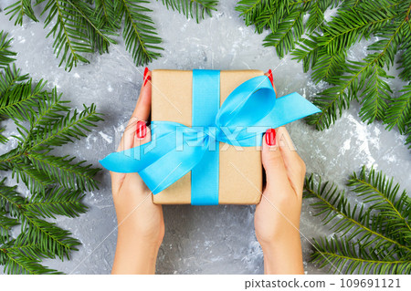womans hand hold the box with gift over grey texture with christmas branches. top vew 109691121