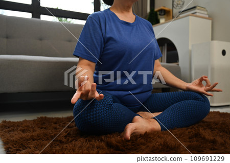 Cropped shot of senior woman sitting in lotus position on carpet during morning meditation in living room 109691229