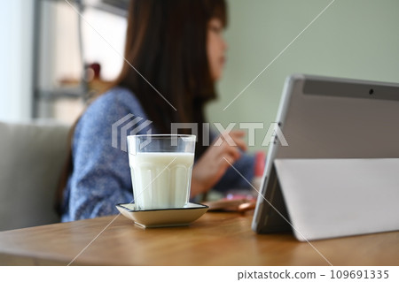 A glass and bottle of milk on wooden table with child girl doing homework on background A glass and bottle of milk on wooden table with child girl doing homework on background 109691335