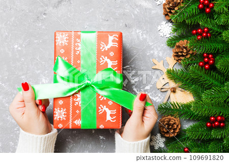 Top view of female hand tie up New Year present on festive wooden background. Fir tree and holiday decorations. Christmas time concept 109691820