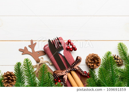 Top view of flatware tied up with ribbon on napkin on wooden background. Christmas decorations and reindeer with empty space for your design. New Year holiday concept Top view of flatware tied up with ribbon on napkin on wooden background. Christmas decorations and reindeer with empty space for your design. New Year holiday concept 109691859
