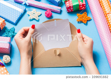 Top view of woman holding an envelope on blue background made of holiday decorations. Christmas time concept Top view of woman holding an envelope on blue background made of holiday decorations. Christmas time concept 109691882