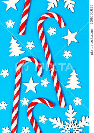 Christmas candy cane lied evenly in row on blue background with decorative snowflake and star. Flat lay and top view Christmas candy cane lied evenly in row on blue background with decorative snowflake and star. Flat lay and top view 109691932
