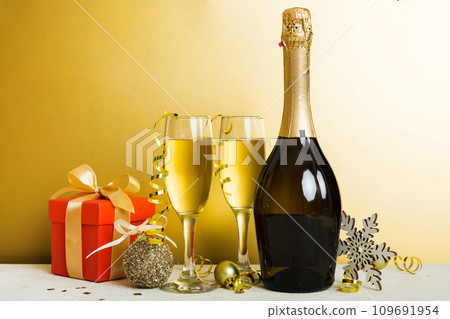 Champagne bottle with confetti, glasses and christmas decor on colored holiday background. Flat lay New Year decorations Champagne bottle with confetti, glasses and christmas decor on colored holiday background. Flat lay New Year decorations 109691954