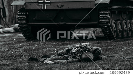 Close Up View On Re-enactor Dressed As German Wehrmacht Soldier Lies Slain In Reconstruction Of Battles World War Ii Near Wehrmacht Light Panzer Tank. German Infantry Soldier. Black And White Close Up View On Re-enactor Dressed As German Wehrmacht Soldier Lies Slain In Reconstruction Of Battles World War Ii Near Wehrmacht Light Panzer Tank. German Infantry Soldier. Black And White 109692489