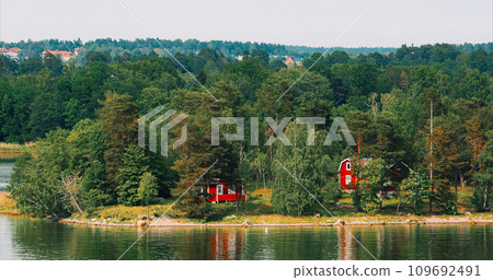 Panoramic View On Many Red Swedish Wooden Sauna Logs Cabins Houses On Island Coast In Summer Cloudy Day. Swedish Old Tradition Wooden Houses. Bold Colors. Travel to Sweden 109692491