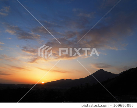 Evening view of Mt. Bandai. The silhouette of the mountains, the orange sun and clouds against the blue sky are impressive and beautiful. 109693093
