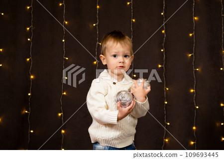 Portrait of a cute two-year-old boy on the background of a bokeh garland at home. Christmas children Portrait of a cute two-year-old boy on the background of a bokeh garland at home. Christmas children 109693445