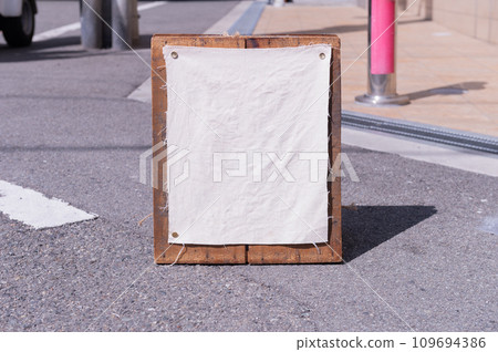 Blank white outdoor advertising stand/sandwich board mock up template. Clear street signage board placed by an outdoor dinning area of a restaurant. Background texture of standee on street. Blank white outdoor advertising stand/sandwich board mock up template. Clear street signage board placed by an outdoor dinning area of a restaurant. Background texture of standee on street. 109694386