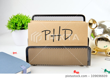 PHD text on paper next to piggy bank, notepad, flower on a white background PHD text on paper next to piggy bank, notepad, flower on a white background 109696609