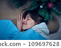 A woman in home clothes sleeps under a decorated Christmas tree 109697628