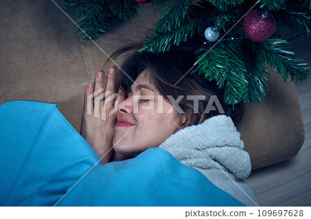 A woman in home clothes sleeps under a decorated Christmas tree A woman in home clothes sleeps under a decorated Christmas tree 109697628