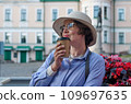 A girl drinks coffee from a paper cup in a coffee shop on the street of an ancient city 109697635