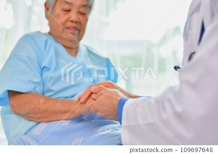 Doctor comforting patient in hospital room. He is holding the hand of a patient in the ward. 109697648