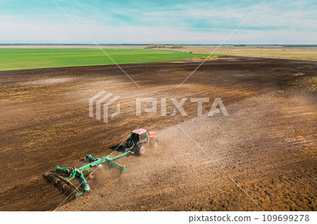 Aerial View. Tractor Plowing Field. Beginning Of Agricultural Spring Season. Cultivator Pulled By A Tractor In Countryside Rural Field Landscape. Dust Rises From Under Plows Aerial View. Tractor Plowing Field. Beginning Of Agricultural Spring Season. Cultivator Pulled By A Tractor In Countryside Rural Field Landscape. Dust Rises From Under Plows 109699278