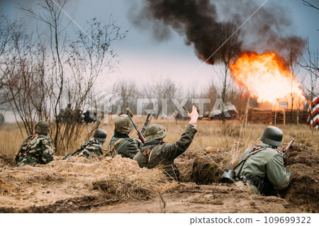 Defensive Position. Re-enactors Armed Rifles And Dressed As World War Ii German Wehrmacht Infantry Soldiers Fighting Defensively In Trench. Building On Fire On Background Defensive Position. Re-enactors Armed Rifles And Dressed As World War Ii German Wehrmacht Infantry Soldiers Fighting Defensively In Trench. Building On Fire On Background 109699322
