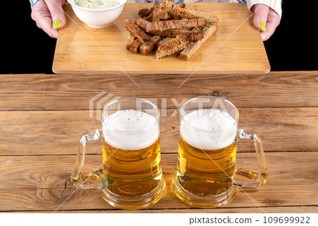 Two glass beer mugs with beer and garlic croutons on a tray in the hands of a girl. 109699922