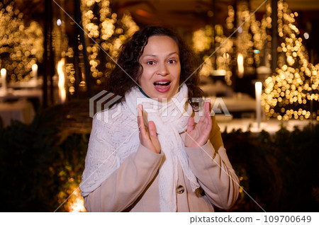 Beautiful woman expressing amazement standing against a city street illuminated with Christmas garlands at night time Beautiful woman expressing amazement standing against a city street illuminated with Christmas garlands at night time 109700649