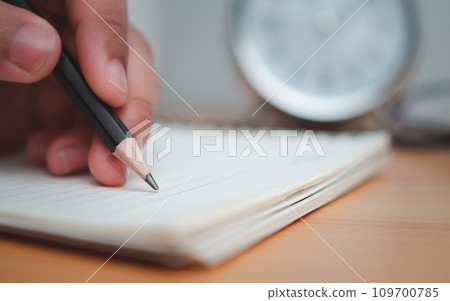 Human hands writing notes with pencil on paper on wooden table surface. 109700785
