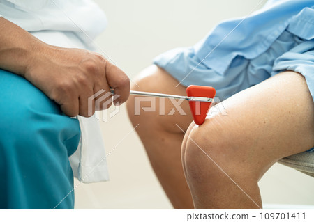 Asian doctor use hammer knock senior woman patient to check knee reflex, nerve and muscle in hospital. 109701411