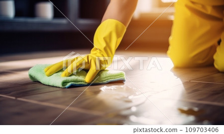 Close-up of hands wearing yellow cleaning gloves as they wipe a tiled floor with a green microfiber cloth. Thorough cleaning at home, household hygiene and daily upkeep concept 109703406