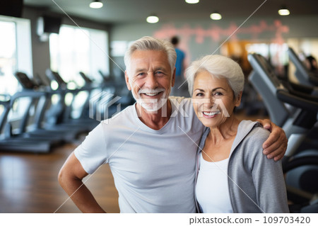 Older smiling couple in modern gym. Faces with happiness and vitality, positive impact of regular exercise on well-being. Background with gym equipment. Active lifestyle and companionship in aging. Older smiling couple in modern gym. Faces with happiness and vitality, positive impact of regular exercise on well-being. Background with gym equipment. Active lifestyle and companionship in aging. 109703420