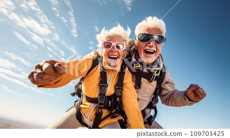 Elated happy senior couple skydiving together. Blue sky with soft clouds background of dynamic motion and adventurous spirit. Adventure in Retirement, Freedom and Vitality in Older Age Elated happy senior couple skydiving together. Blue sky with soft clouds background of dynamic motion and adventurous spirit. Adventure in Retirement, Freedom and Vitality in Older Age 109703425