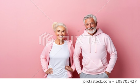 Elderly couple aktive seniors in pink hoodie stands smiling against soft pink background. They both exemplify active and joyful healthy aging. Senior Fitness. 109703427