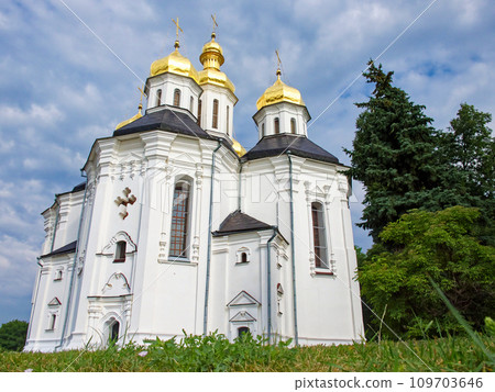 The Orthodox Church of St. Catherine, a resplendent white church with gilded domes and crosses, as it stands in perfect harmony with the surrounding lush greenery and the tranquil blue sky. The Orthodox Church of St. Catherine, a resplendent white church with gilded domes and crosses, as it stands in perfect harmony with the surrounding lush greenery and the tranquil blue sky. 109703646