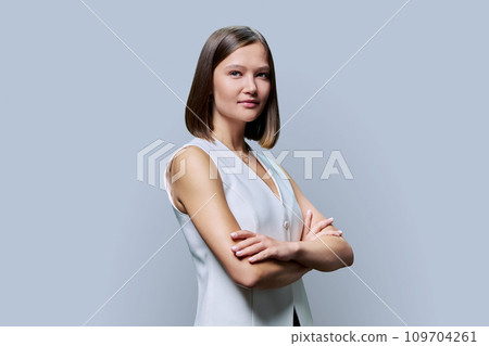 Young confident woman with crossed arms looking at camera on gray background Young confident woman with crossed arms looking at camera on gray background 109704261