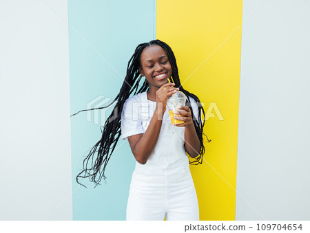 Happy girl in white clothes holding a cocktail and having fun while standing outdoors Happy girl in white clothes holding a cocktail and having fun while standing outdoors 109704654