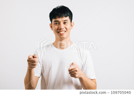 A cheerful Asian man excitedly makes a two-gun gesture to the camera with a friendly and cheeky expression. Isolated on white background, he exudes positivity and joy. 109705040