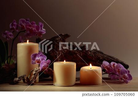 Orchid flowers and burning candles on a background of old wooden snags. Orchid flowers and burning candles on a background of old wooden snags. 109705060