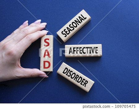 Sad - Seasonal Affective Disorder symbol. Wooden blocks with words Sad. Businessman hand. Beautiful deep blue background. Business and Sad concept. Copy space. 109705475